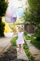 Funny girl child toddler with two tails with balloons outside. Balloons of pastel delicate colors