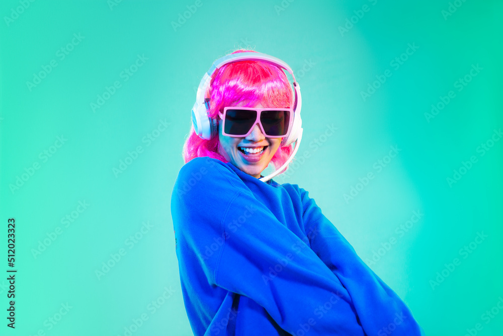 Wall mural Young asian woman in blue sweatshirt pink short hair punk style wearing sunglasses and headphones posing dancing on the green screen background.