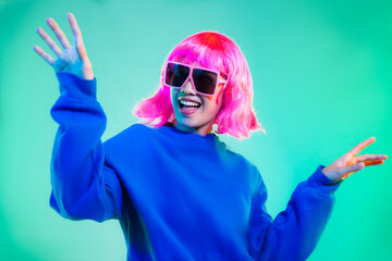 Young asian woman in blue sweatshirt pink short hair punk style wearing sunglasses posing dancing on the green screen background.