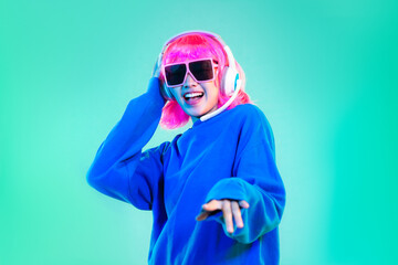 Young asian woman in blue sweatshirt pink short hair punk style wearing sunglasses and headphones posing dancing on the green screen background.