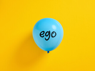 Inflated blue balloon with the word ego and a pin. Selfishness or inflated extreme ego