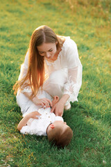 Mom tickles her son lying on the grass. Blooming garden in spring.