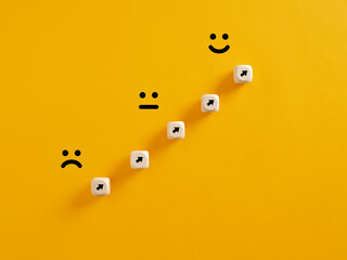 Arrows on wooden cubes pointing from a sad expression towards a happy one. Personal growth and...
