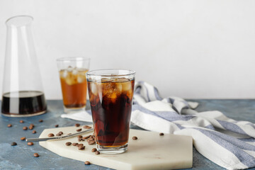 Glass of cold brew and coffee beans on color table against white background