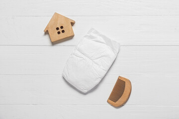 Baby diaper, hair comb and toy house on white wooden background