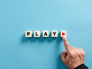 Male hand presses the play button with the word play on wooden cubes.