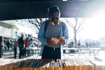Young man reading book at street market on sunny day