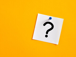 Handwritten question mark on a note paper pinned on a yellow board. Confusion, doubt, mystery, asking or problem
