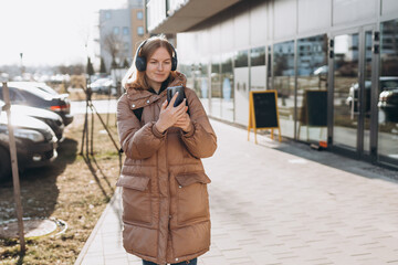 Young woman listening music in headphones in the city. Happy woman with backpack walking on the street. Urban lifestyle concept. Traveler. Spring time.