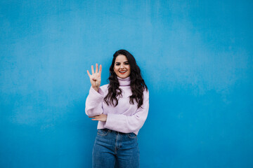 Smiling young beautiful woman showing number 4 in front of blue wall