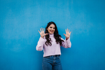 Smiling young beautiful woman showing number 10 in front of blue wall
