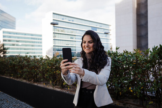 Smiling young businesswoman taking selfie at financial district