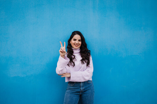 Smiling young beautiful woman showing number 2 in front of blue wall