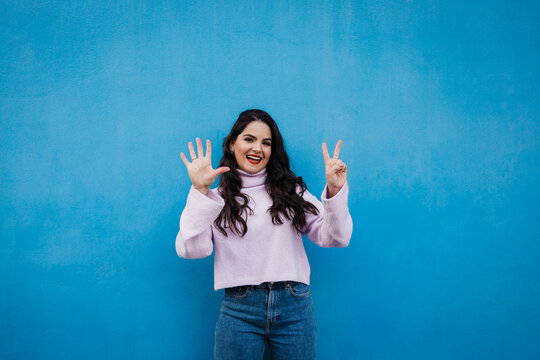 Smiling young beautiful woman showing number 7 in front of blue wall