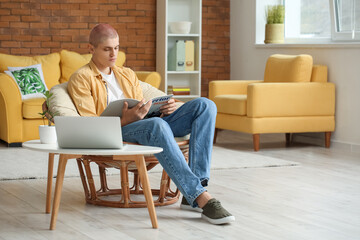 Young guy reading magazine in armchair at home