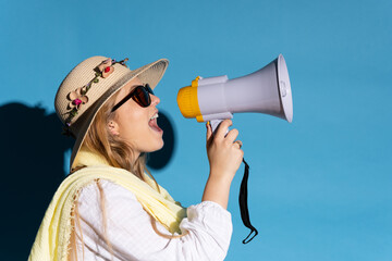 Side view of young tourist woman shouting on megaphone isolated on blue background.