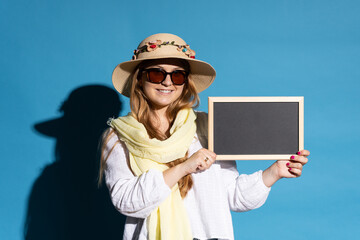 Young tourist woman holding blackboard with copy space isolated on blue background.