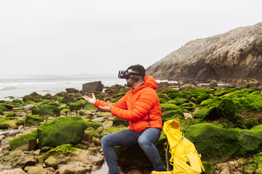Man wearing virtual reality simulator gesturing sitting on rock
