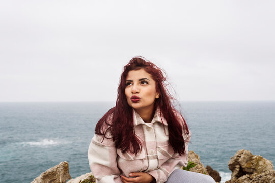 Woman with red hair puckering lips sitting on rock