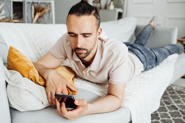 A man lying on the couch reads the news on a smartphone