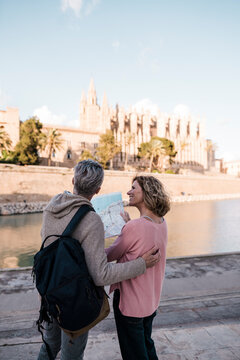 Mature tourists examining map by sea in city on vacation