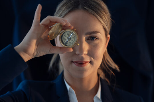 Businesswoman holding compass in front of eye against black background