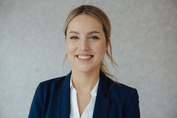 Smiling beautiful blond businesswoman in front of gray wall