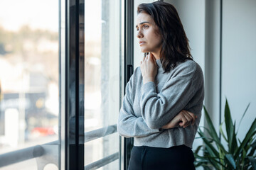 Thoughtful sad woman looking through window at home