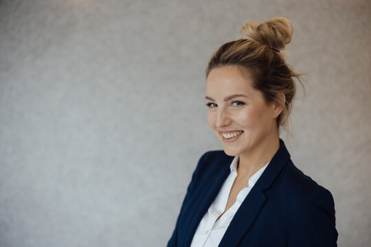 Happy businesswoman with blond hair bun in front of gray wall