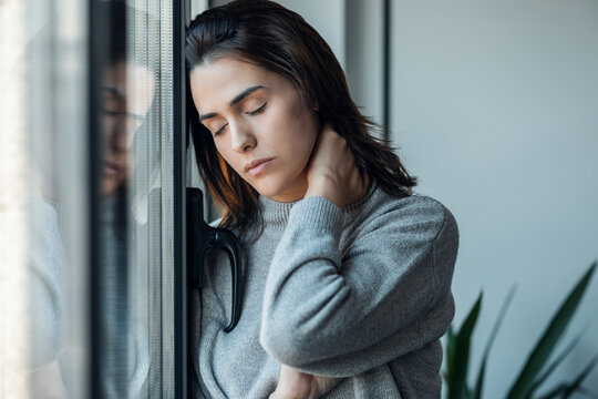 Tired woman with eyes closed standing by window at home