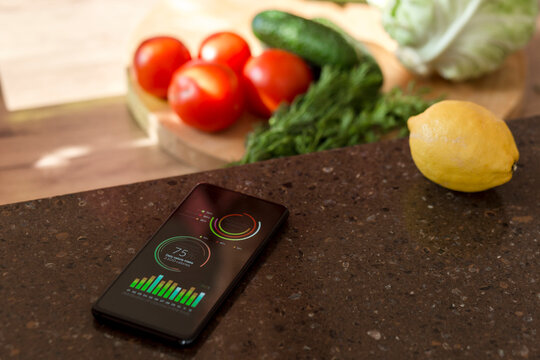 Smartphone with charts on kitchen counter next to vegetables