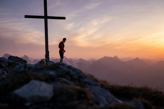 Hiker standing by summit cross on mountain