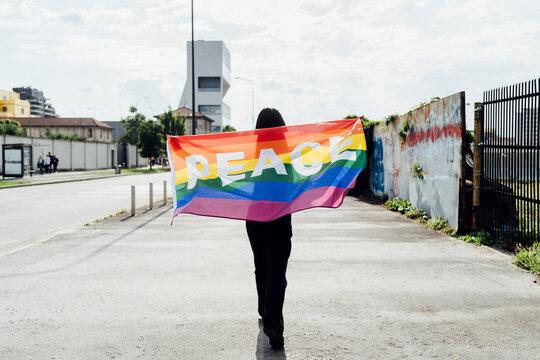 Young woman with rainbow flag walking on road
