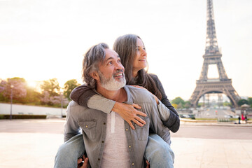 Smiling mature man giving piggyback ride to woman in front of Eiffel Tower, Paris, France