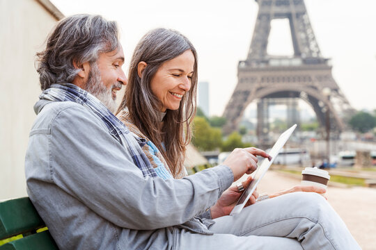 Smiling mature woman with man using tablet PC sitting on bench near Eiffel Tower, Paris, France