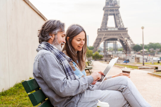 Happy woman with man using tablet PC sitting on bench near Eiffel Tower, Paris, France