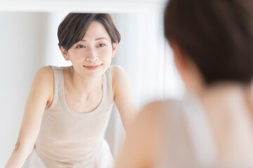 朝、洗面所で鏡を見ながら微笑むアジア人女性