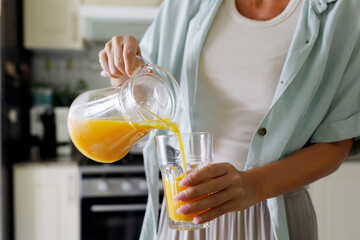 Hands of woman pouring fresh orange juice in glass from jug