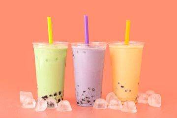 Plastic cups of tasty bubble tea and ice cubes on color background