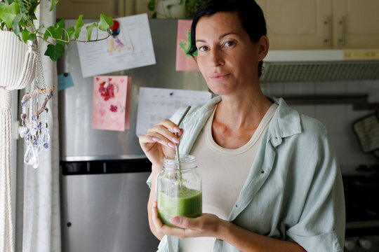 Woman drinking celery smoothie from mason jar at home