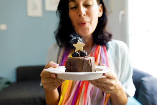 Smiling woman blowing out star shape birthday candle on cake at home