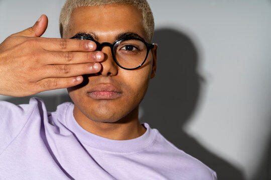 Young man covering eye with hand standing in front of wall