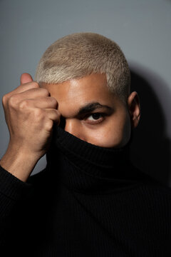 Young man covering face with turtleneck top against gray background