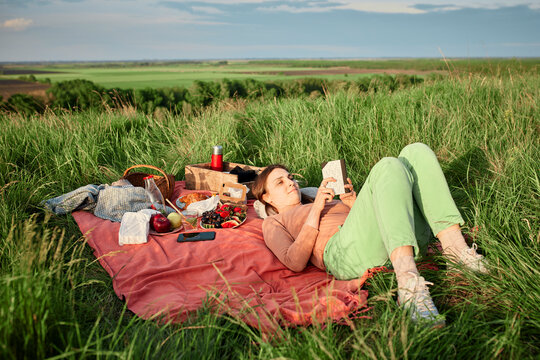 Smiling woman reading book at picnic in field