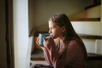 Girl pre teenager with cup of tea on stairs of house, pensive calm child, dark style
