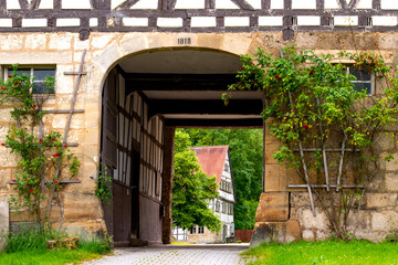 Historic monastery farmhouse from 13th century with picturesque courtyard entry and half timbered facade. Tourist attraction near  “Uracher Wasserfall“ cascade in idyllic rural landscape in Germany.