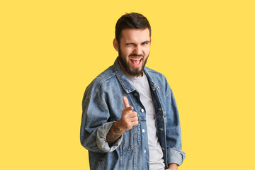 Smiling man pointing at viewer and winking on yellow background