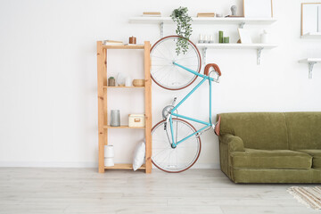 Shelf unit with stylish decor, bicycle and sofa near white wall in living room