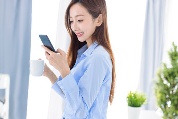 Young  businesswoman drinking coffee and watching the smart phone  in office