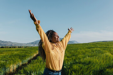 Happy young woman with arms raised in meadow